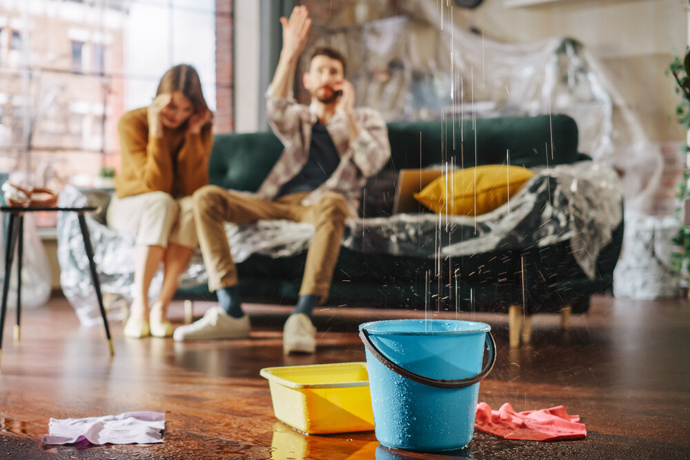 Family Sitting On Couch, Upset, Watching Water Leak From Ceiling