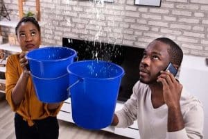 Couple with buckets catching water leaking from roof