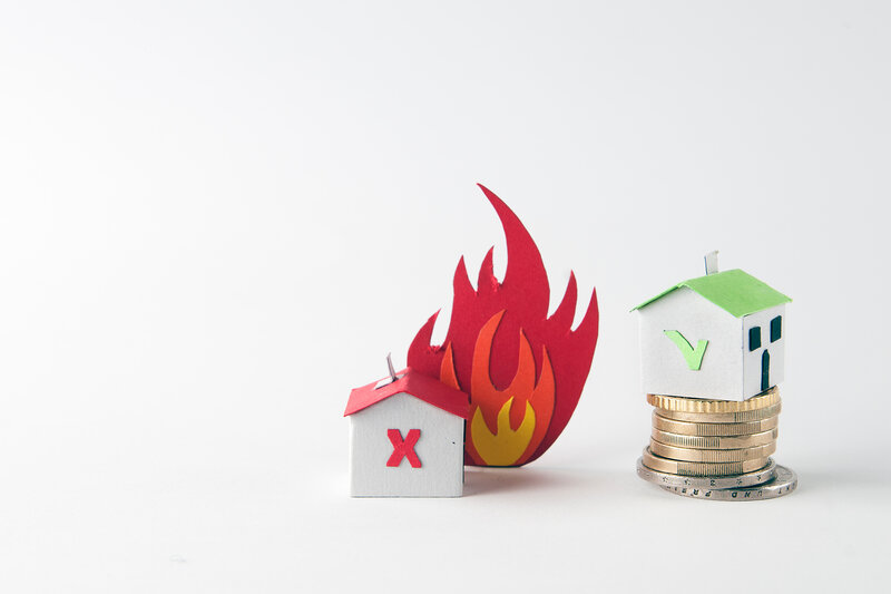 A paper house that burns and a safe house over a coin pile: fire insurance concept