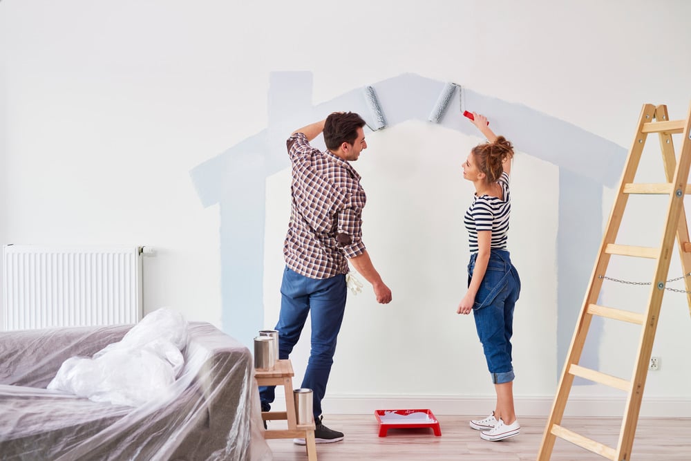 Man And Woman Adding A Coat Of New Paint, The Part They'Ve Done Already Is The Outline Of A House