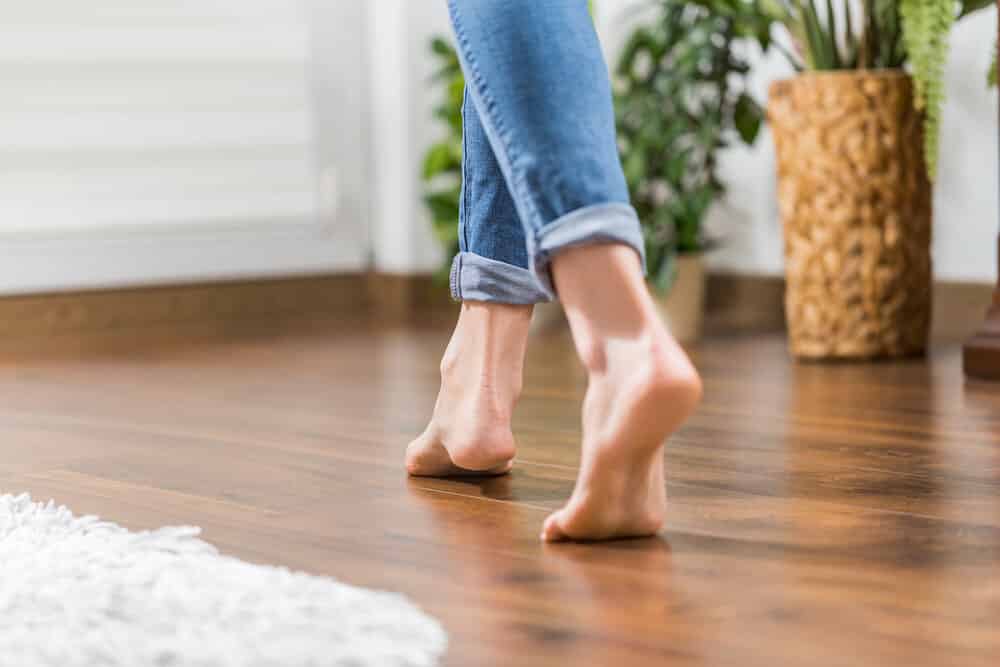 Young woman walking in the house on the warm floor. Gently walked the wooden panels. Article about how to extend the lifespan of hardwood floors