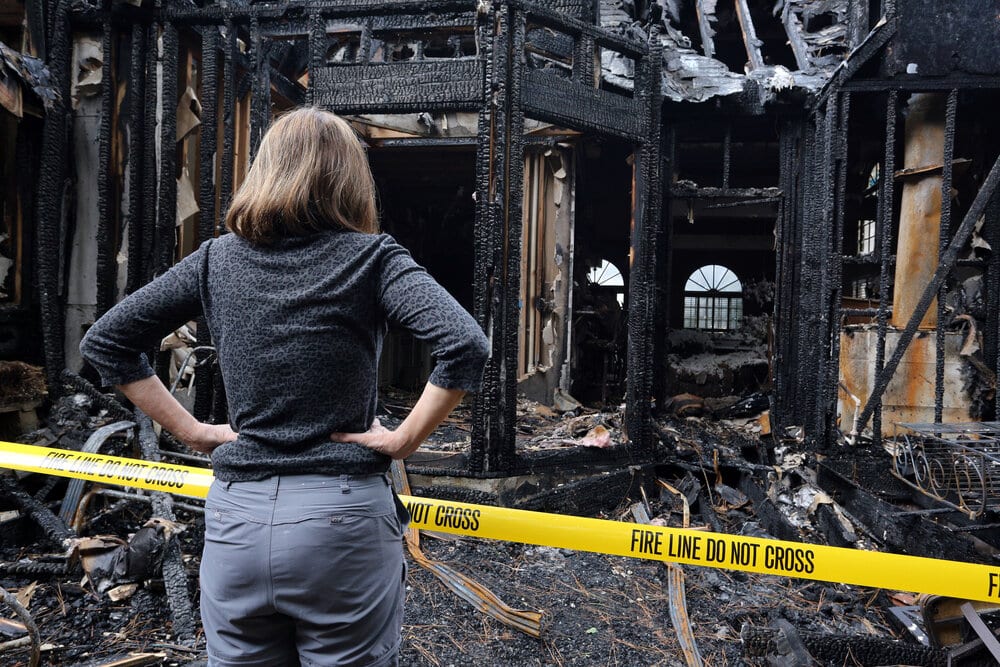 Woman standing outside her house after a fire, wondering if she save damaged items