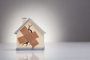 Broken House Model With Crossed Band Aid On Desk