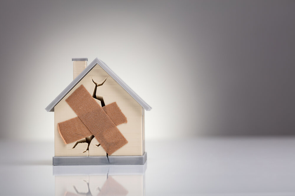 Broken House Model With Crossed Band Aid On Desk