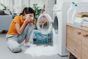 Woman checking her damaged washing machine, the floor is flooded